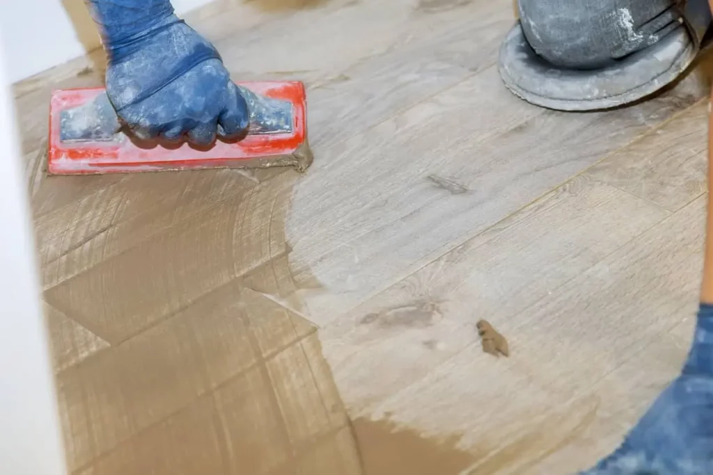 Un carreleur pose le coulis de céramique sur un plancher de carrelage imitation bois franc.