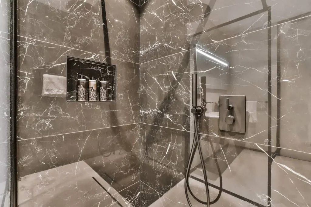 Douche à l'italienne en carrelage marbré avec paroi vitrée et niche sur le mur.